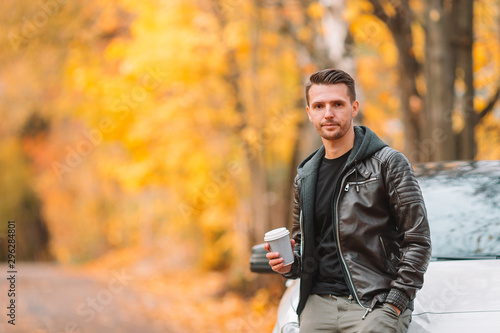 Young man drinking coffee with phone in autumn park outdoors