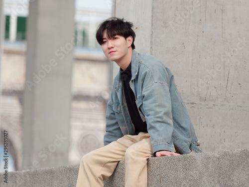Portrait of a handsome Chinese young man in jeans sitting and smiling at camera.