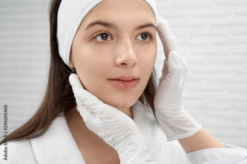 Cosmetologist in white gloves inspecting face of patient. Cosmetologist in white gloves inspecting face of patient.