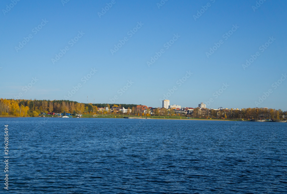 Beautiful blue lake with clear sky. Autumn yellow forest in the distance on the horizon.
