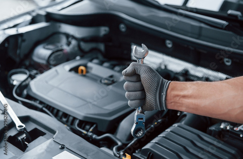 Everything will be fixed. Man's hand in glove holds wrench in front of broken automobile