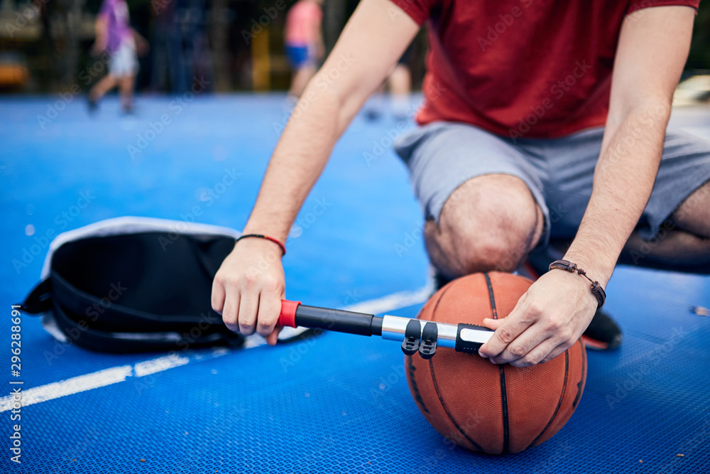 Man inflating basketball ball with a hand pump on the urban court.