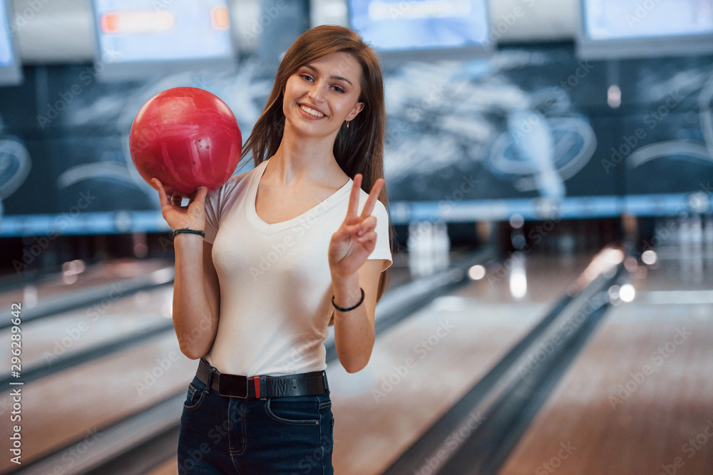 Φωτογραφία Cheerful young woman in casual clothes holding red bowling ball in the club