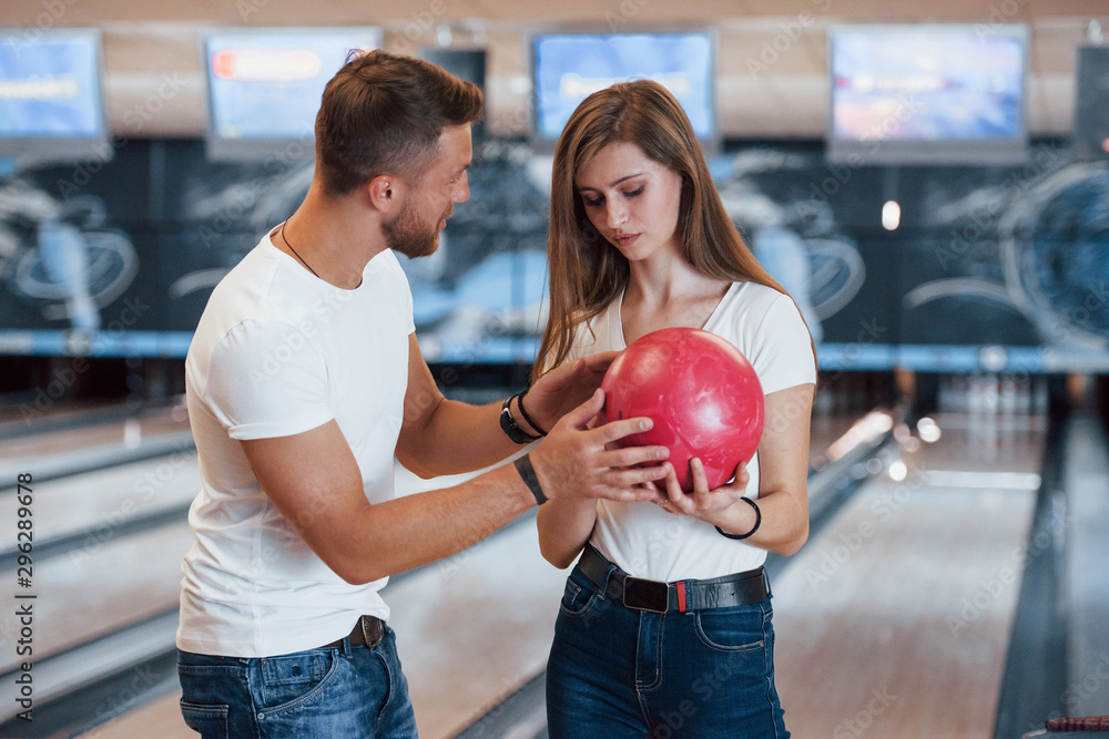 Φωτογραφία Man teaching girl how to holds ball and play bowling in the club