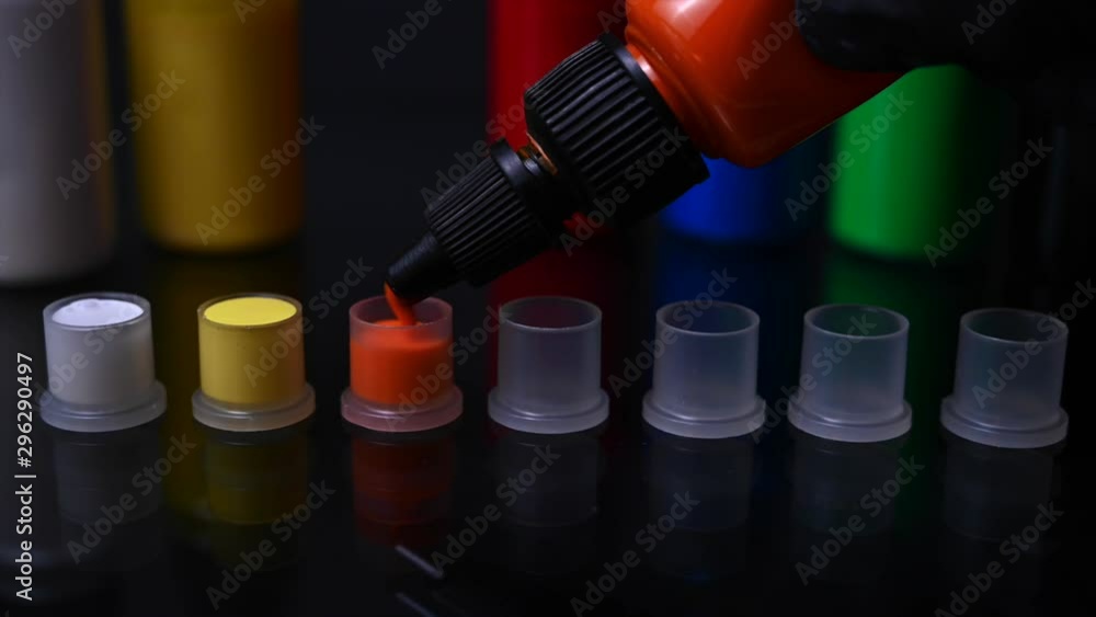 Closeup of tattoo artist pouring orange ink in cap Closeup of tattoo artist pouring orange ink in cap