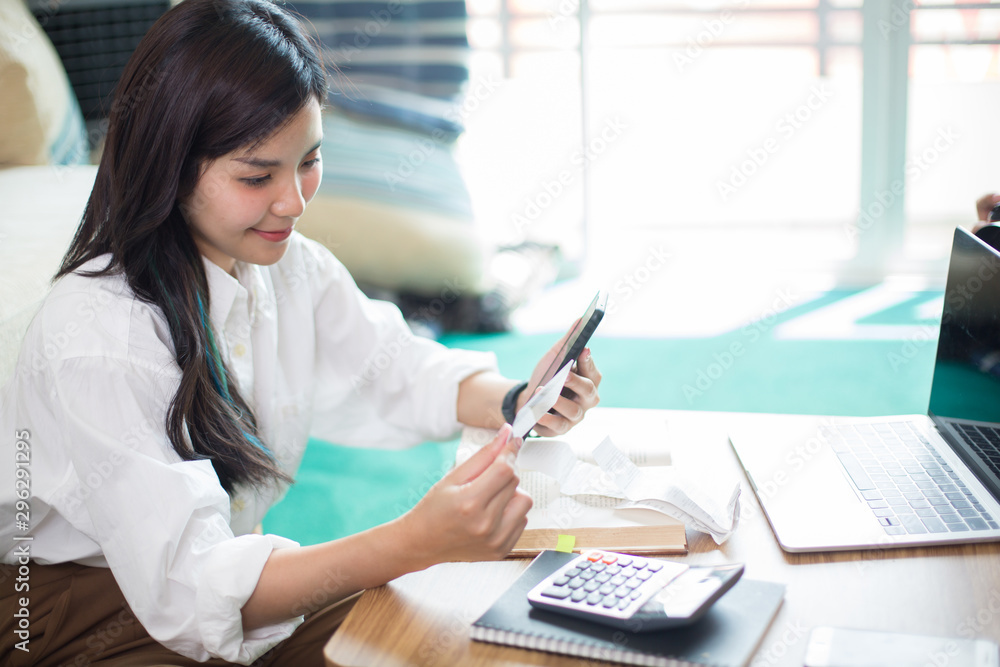 Young Asia women are using computers, books, phones, bills, cash and calculators. Online Inside her house Young Asia women are using computers, books, phones, bills, cash and calculators. Online Inside her house