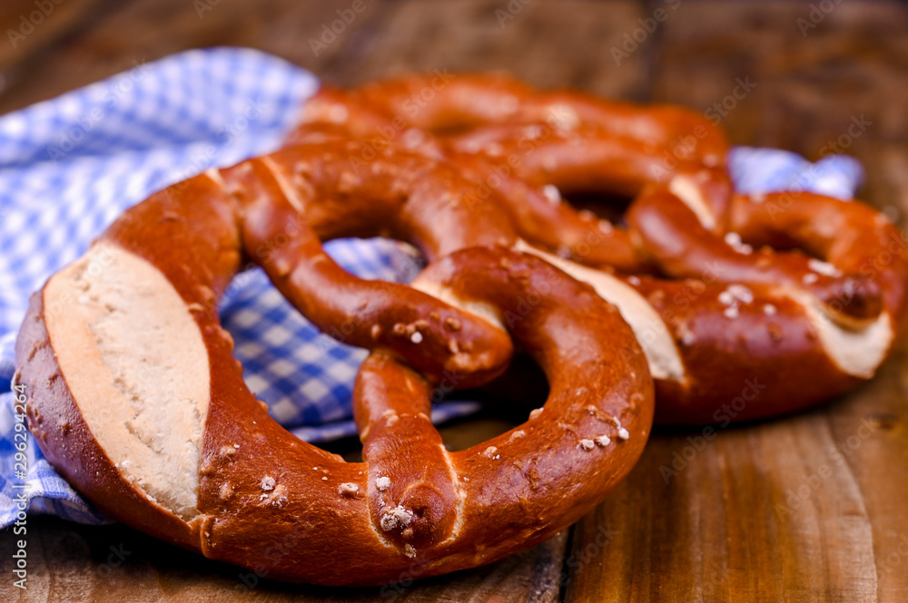 Bavarian pretzel decorated with a blue and white cloth on a rustic wooden board - Munich Oktoberfest. Background and free space for text. Traditional pastries for the festival.Close-up. Bavarian pretzel decorated with a blue and white cloth on a rustic wooden board - Munich Oktoberfest. Background and free space for text. Traditional pastries for the festival.Close-up.