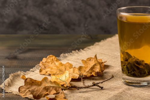 Hot green tea in a glass and autumn leaves on a dark background. Antioxidant and toxin-removing tea after spa,
