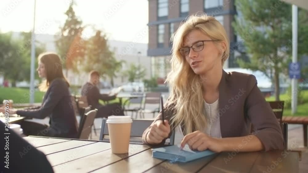 Medium shot of young blonde woman in eyeglasses talking to black male colleague and discussing work with him over cup of coffee outdoors Medium shot of young blonde woman in eyeglasses talking to black male colleague and discussing work with him over cup of coffee outdoors