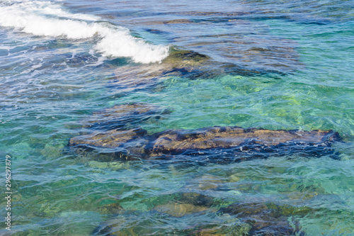 a wave runs over the rocky shore. clear turquoise water