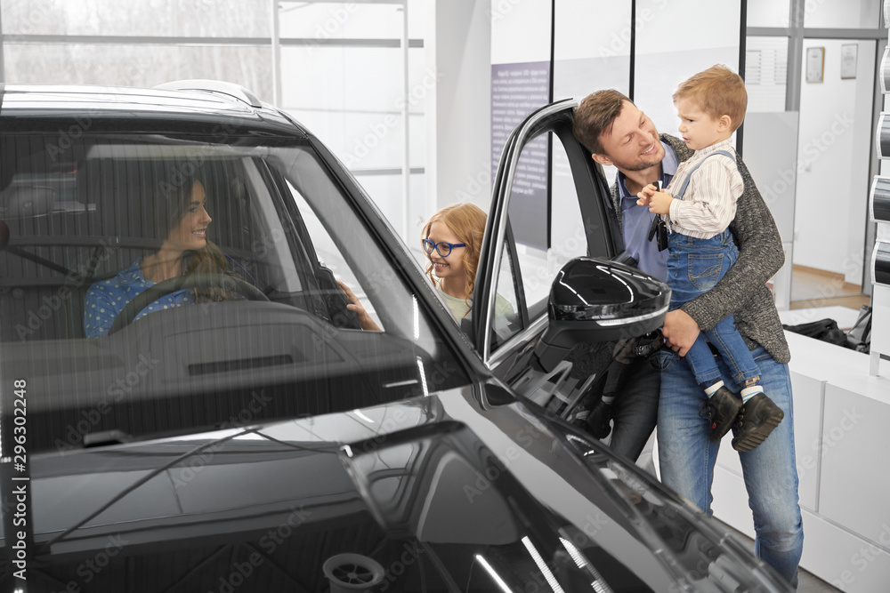 View from side of happy family looking at car in auto salon View from side of happy family looking at car in auto salon