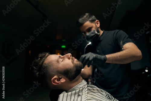 Side view of man sitting at salon and doing beard shaving