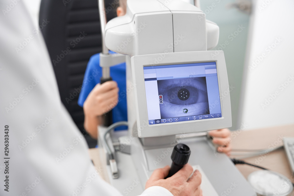 Fototapeta premium Clever male oculist using machine for checking eye sight