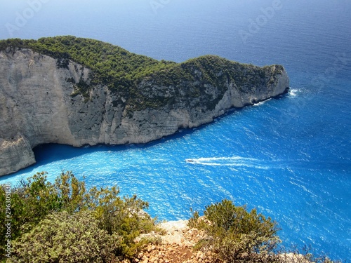 Small boat going to Navagio bay, Navagio beach and ship wreck. The most famous natural landmark of Zakynthos, Greece, Europe. Amazing aerial view from the view from a wild slope and rocks.