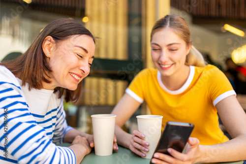 mother laughing at daughters mobile phone while sitting at cafe