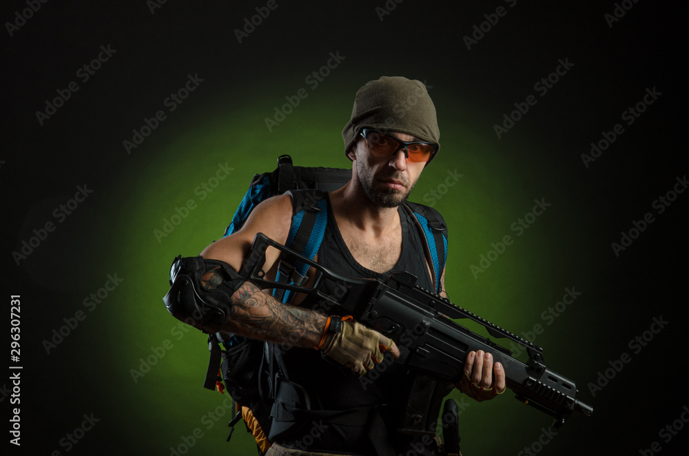 a man with a gun and a backpack on a dark background with emotions looking, aiming, watching, sneaking