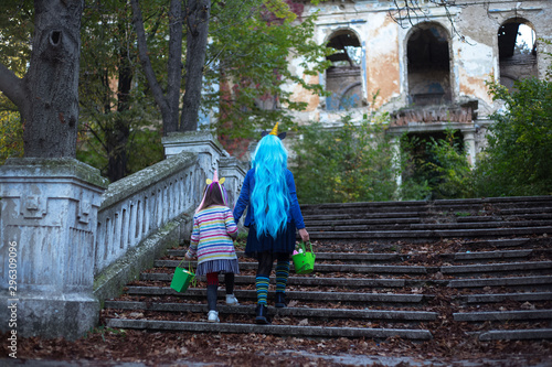 Back view of two little girls in halloween costume of unicorn, with halloween bucket, walking up stairs to scary abandoned house. © Lalandrew