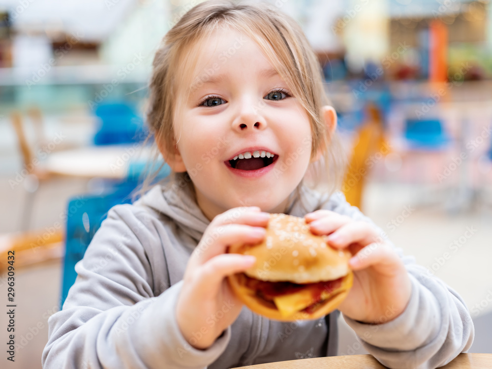 Cute little girl eating fast food hamburger in cafe Cute little girl eating fast food hamburger in cafe