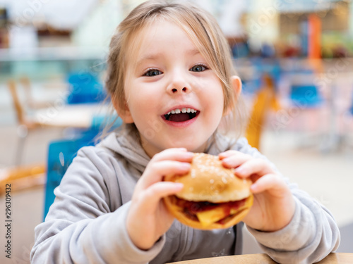 Cute little girl eating fast food hamburger in cafe