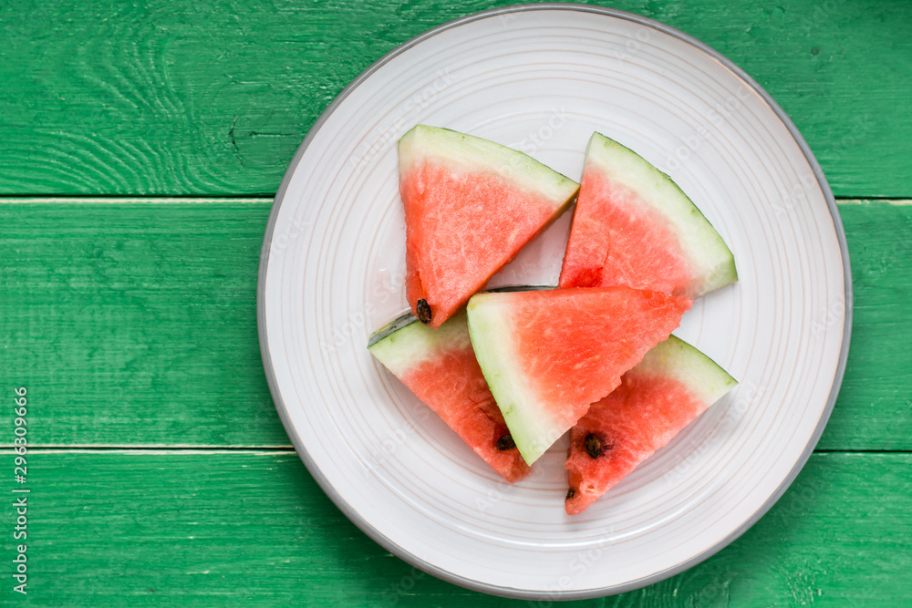 Sliced watermelon on a plate and uncut watermelon on a green wooden table. Top view Sliced watermelon on a plate and uncut watermelon on a green wooden table. Top view