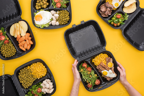 cropped view of woman holding eco package with corn, meat, fried eggs and salad isolated on yellow