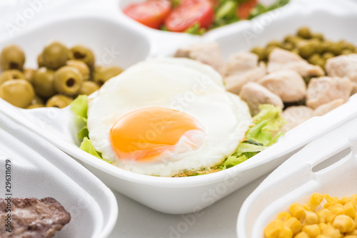 selective focus of eco package with vegetables, meat, fried egg and salad on white background
