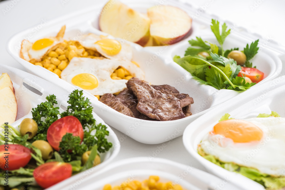 selective focus of eco packages with apples, vegetables, meat, fried eggs and salad on white background selective focus of eco packages with apples, vegetables, meat, fried eggs and salad on white background