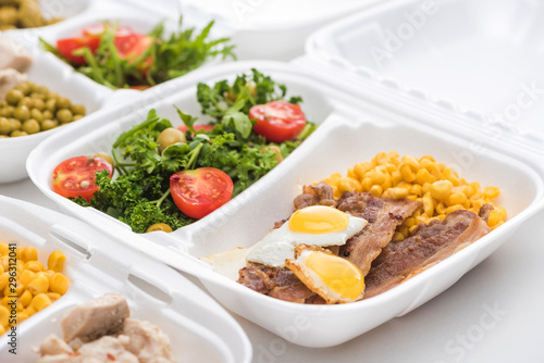 selective focus of eco package with corn, meat, fried eggs and salad on white background