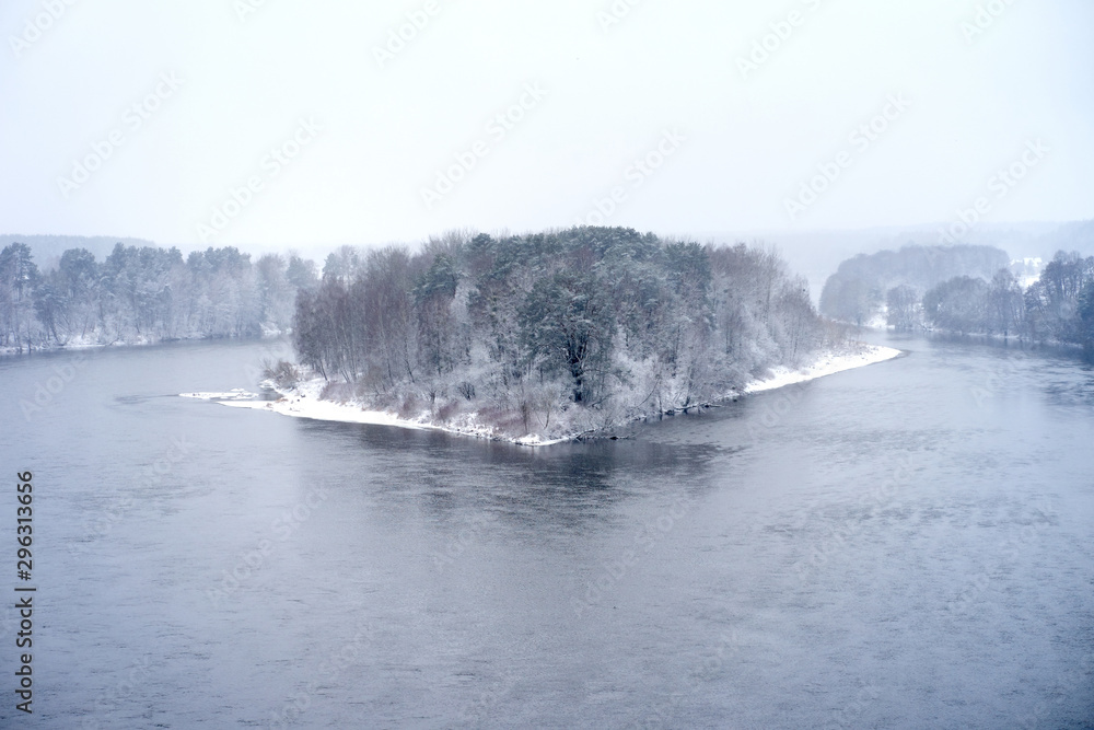 Snow-covered island of winter forest among river