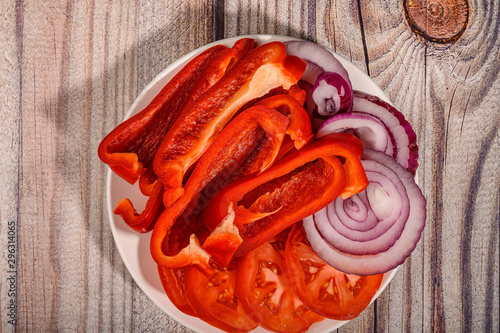 Sliced tomatoes, sweet peppers and onions in a plate on a wooden table.
