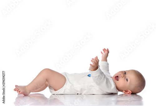 Laughing infant baby toddler in white bodysuit is lying on his back, holding hands up, waving, happy screaming on white