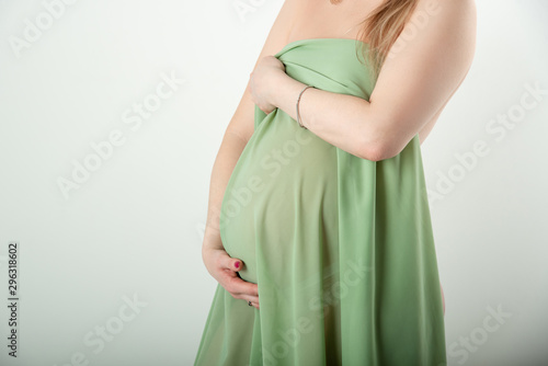 Beautiful pregnant girl is standing and holding her stomach in a green cloth on a white background