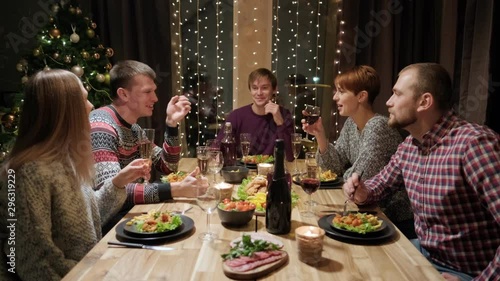 Friends holiday party dinner at home around the table. Celebrate Christmas. Five people eat, drink champagne, talk and laugh. Christmas eve.