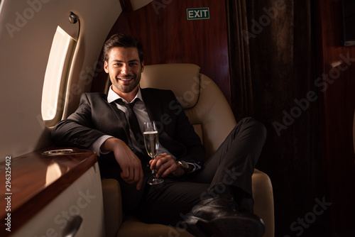 handsome smiling man holding glass of champagne in plane