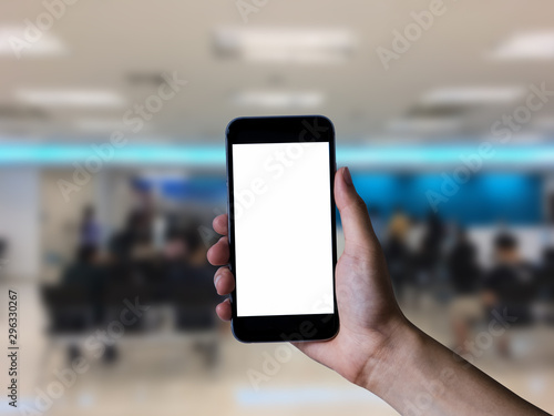 Hand holding white mobile phone with blank white screen in bank.