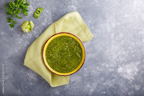 Tomatillo salsa verde. Bowl of spicy green sauce on gray table, mexican cuisine. photo