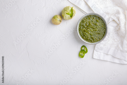 Tomatillo salsa verde. Bowl of spicy green sauce on white table, mexican cuisine. Top view. Copy space. photo