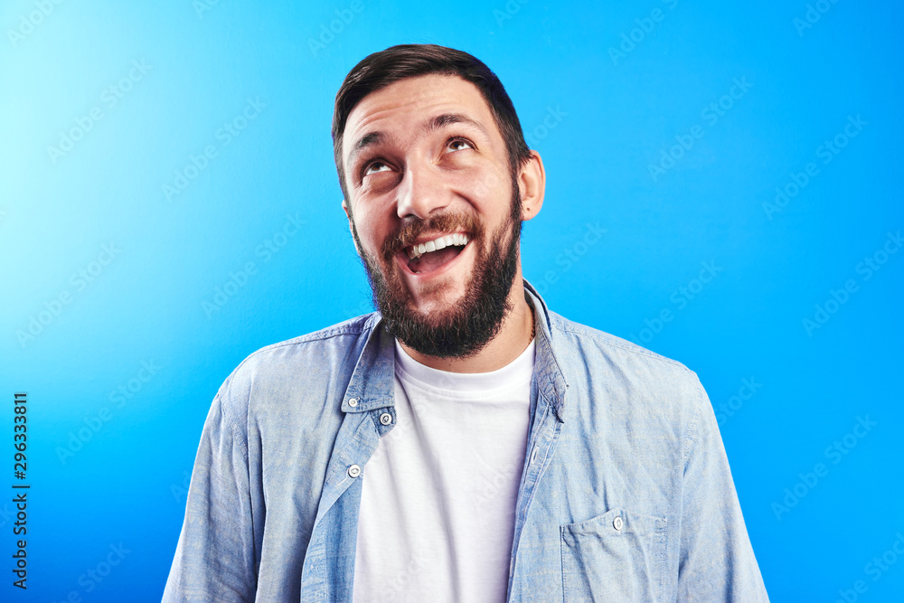 Portrait of toothy smiling and joyfully laughing handsome caucasian brutal bearded man dressed in casual isolated on blue background Portrait of toothy smiling and joyfully laughing handsome caucasian brutal bearded man dressed in casual isolated on blue background
