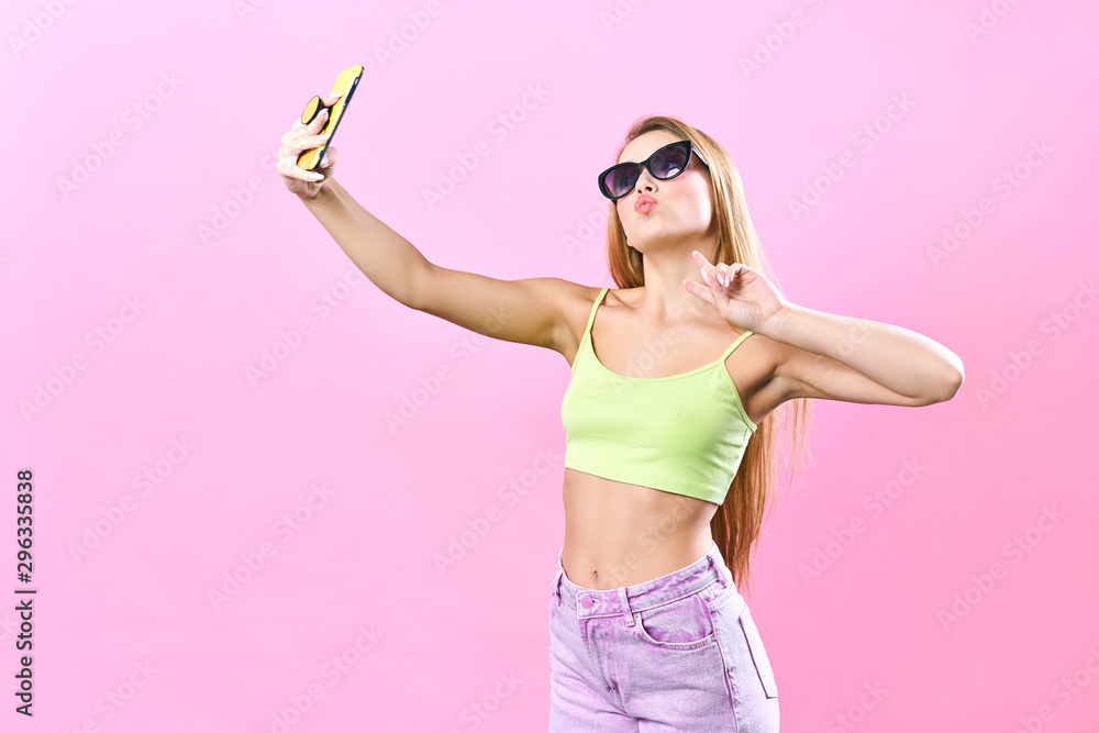 Close-up portrait of young cheerful readhead woman in summer wear makes selfie on smartphone, over pink background Close-up portrait of young cheerful readhead woman in summer wear makes selfie on smartphone, over pink background