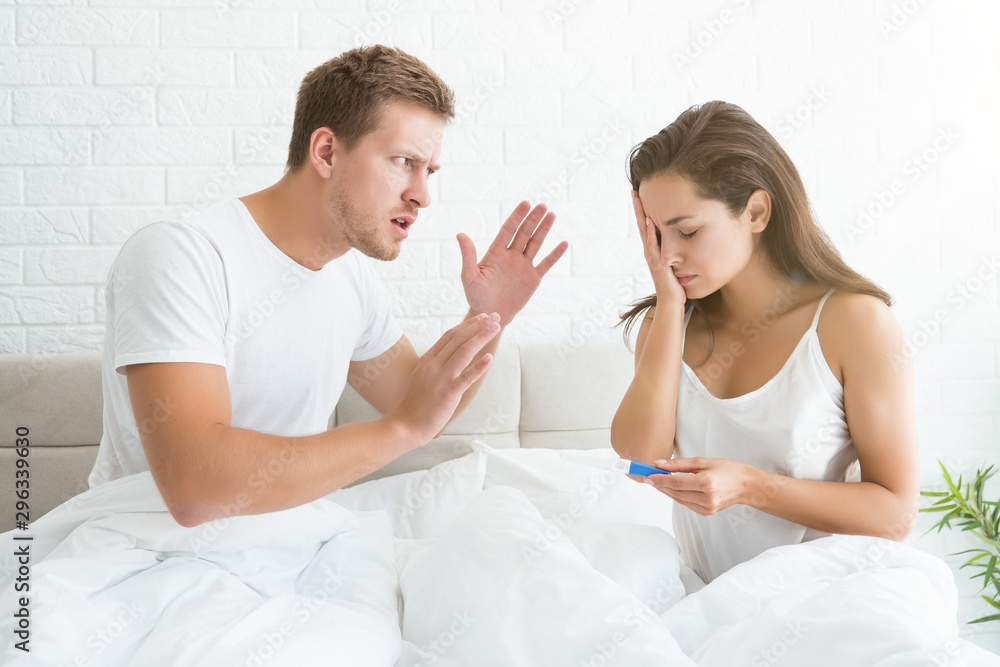 young couple quarrelling handsome man crying at young beautiful woman who is holding pregnancy test young couple quarrelling handsome man crying at young beautiful woman who is holding pregnancy test
