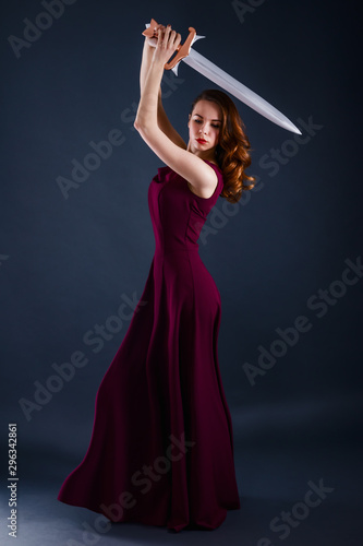 Beautiful young princess in a long dress defending herself with a sword