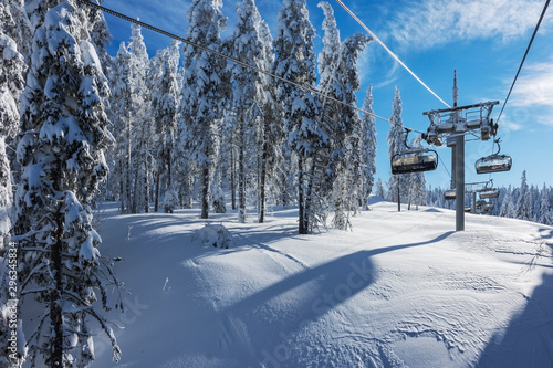 Sunny morning in the Rhodope Mountains, ski resort Pamporovo. Chair ski lift over pine trees. Snejanka TV tower in  background. Sports and recreation concept. Selective focus.