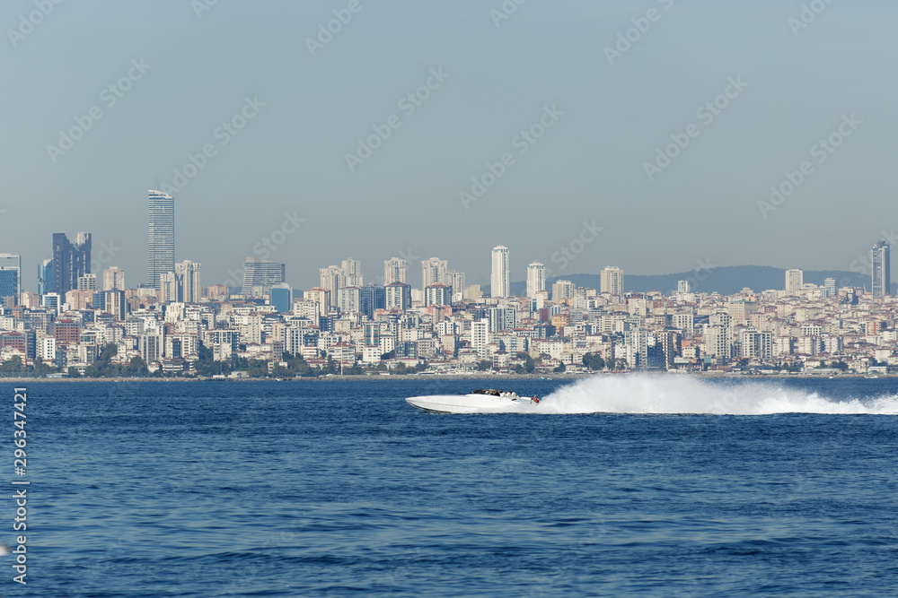 Cigarette racing speed boat moving fast off-shore near to Prince Islands in Marmara Sea of Istanbul. Urban cityscape with skyline and buildings in the background.