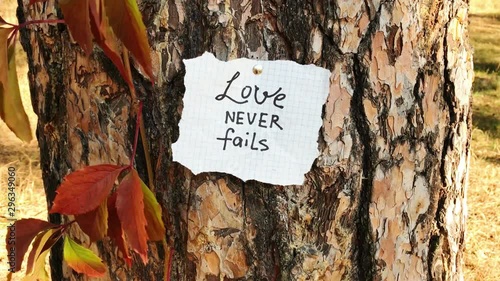 Love never fails - card with biblical quote, christian lettering on paper on nature