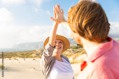 Smiling young couple giving high five on seashore. Happy spouse during summer holiday. Relationship concept
