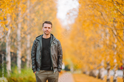 Young man drinking coffee with phone in autumn park outdoors