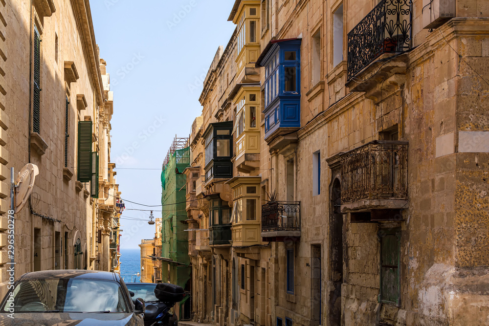 Residential house facade with traditional Maltese multicolored enclosed wooden balconies in Valletta, Malta, with sea at background. Authentic Maltese urban scene.