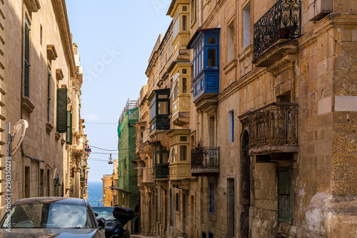 Residential house facade with traditional Maltese multicolored enclosed wooden balconies in Valletta, Malta, with sea at background. Authentic Maltese urban scene.