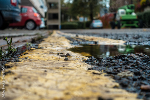 A low angle, shallow depth of field view of a puddle at the edge of a road with painted double yellow lines running through it.
