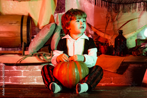 Funny kid in carnival costumes indoors. Children in America celebrate Halloween. Halloween decorations. Cheerful child with pumpkins and candy.